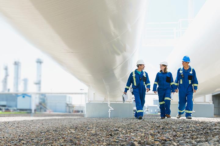 three workers walking below pipes at gas plant